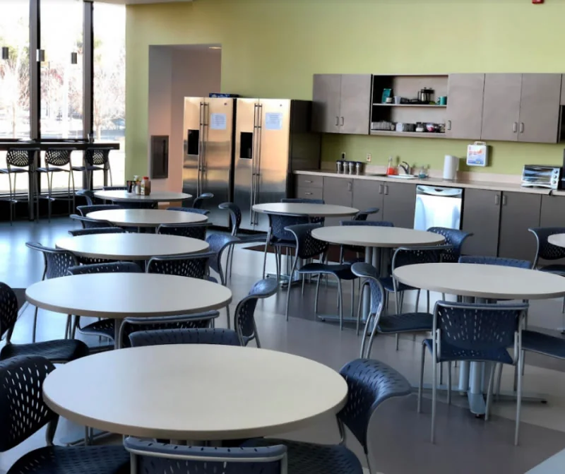 Commercial break room with tables, chairs, refrigerators and a kitchen counter.