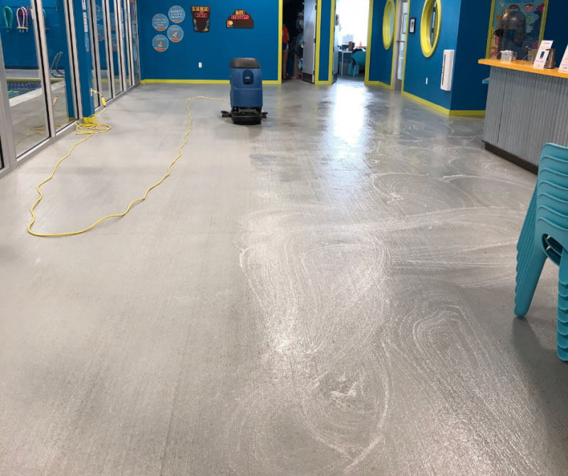 Floor-cleaning machine on a gray floor in a blue-walled reception area.