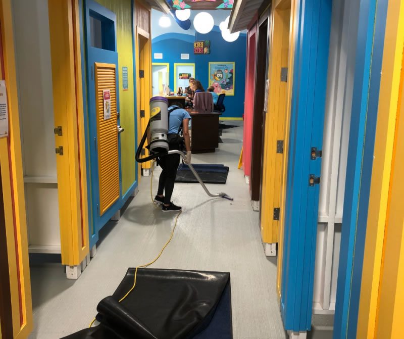 Cleaner using a backpack vacuum along an interior corridor.