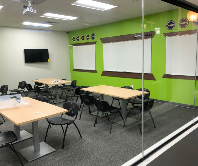 Training room with tables, chairs and whiteboards behind a glass wall.