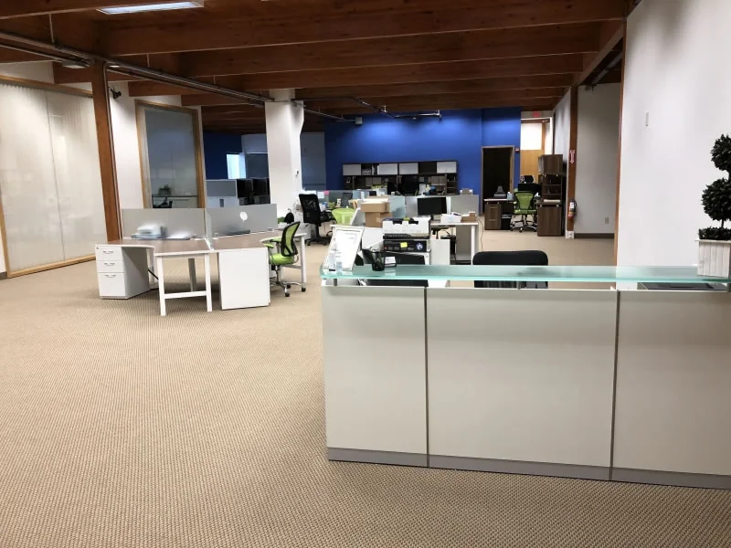 Open office with white desks, green chairs, exposed ceiling beams and a blue wall.