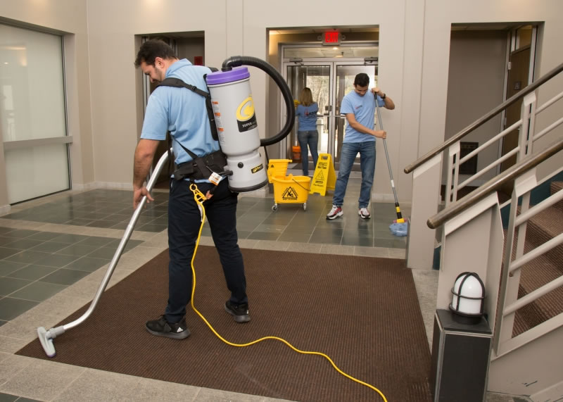 Cleaners vacuuming and mopping a commercial entrance lobby.