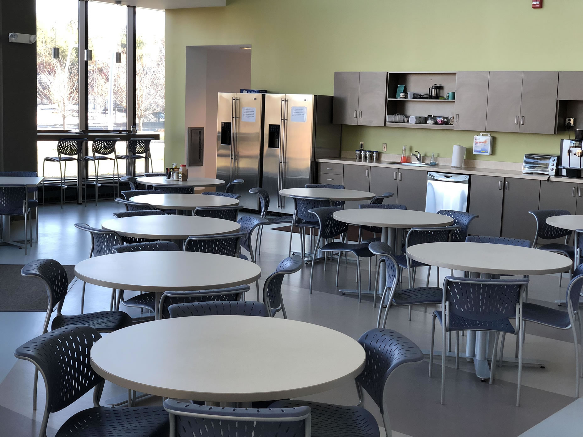 Commercial break room with round tables, chairs, refrigerators and a kitchen counter.